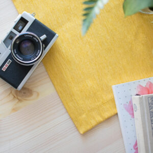 Photo of a camera laying on top of a desk with a bright yellow cloth underneath it