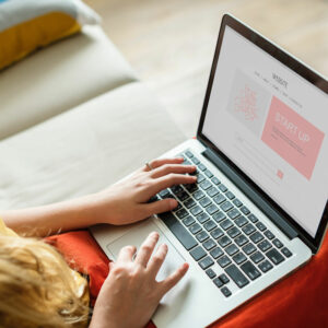 Photo of a woman on a couch typing on an open laptop