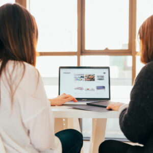 Photo of two women sitting together looking at an open laptop screen