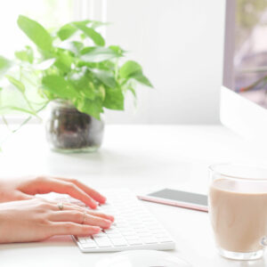 Photo of hands typing on a keyboard with a cup of coffee and plant on the desk