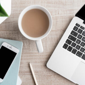 Overhead photo of a cup of tea, laptop keyboard, phone, and book