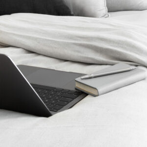 Photo of an open laptop and notebook laying on a gray bedspread