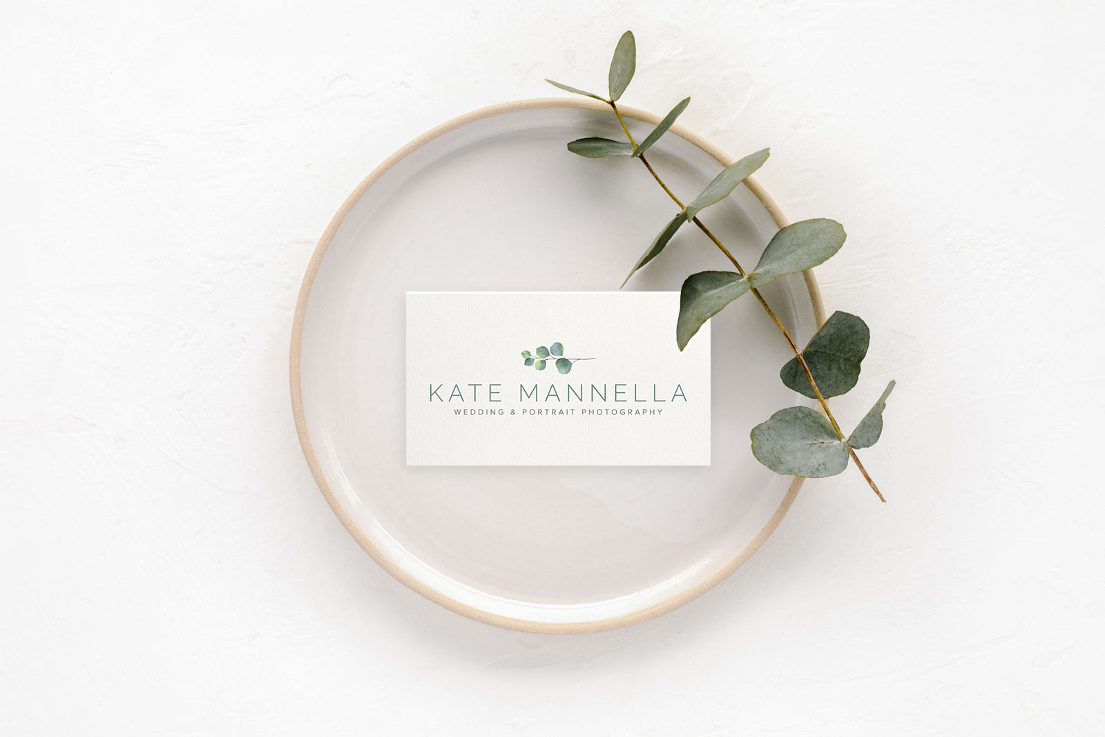 Photo of a plate with an elegantly designed business card laying on top, with a piece of eucalyptus off to the side